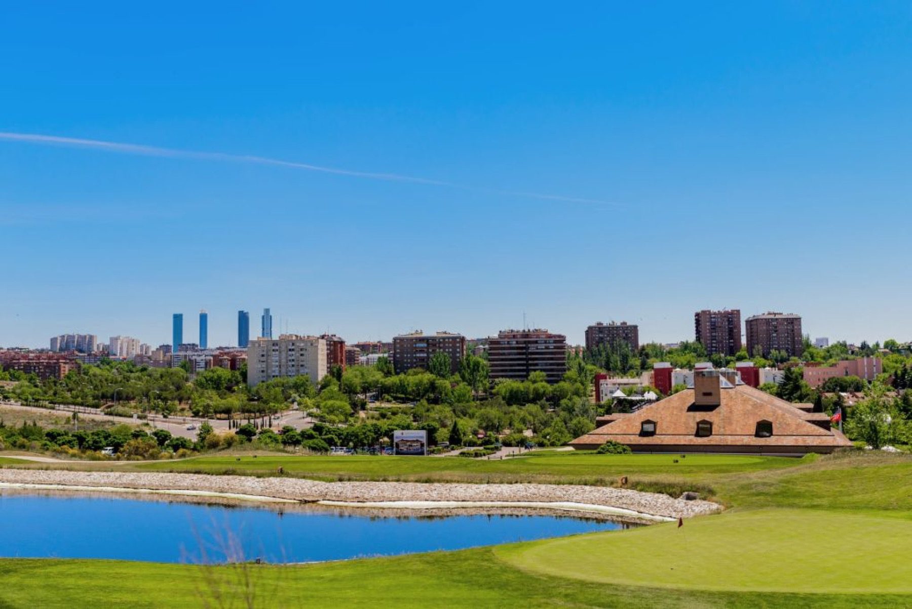 Green and lake at Centro Nacional with the Madrid skyline behind: selling a golf trip to Madrid by corridor